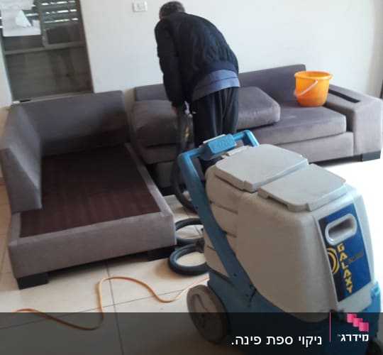 אדם מנקה ספה עם מכונת ניקוי מקצועית